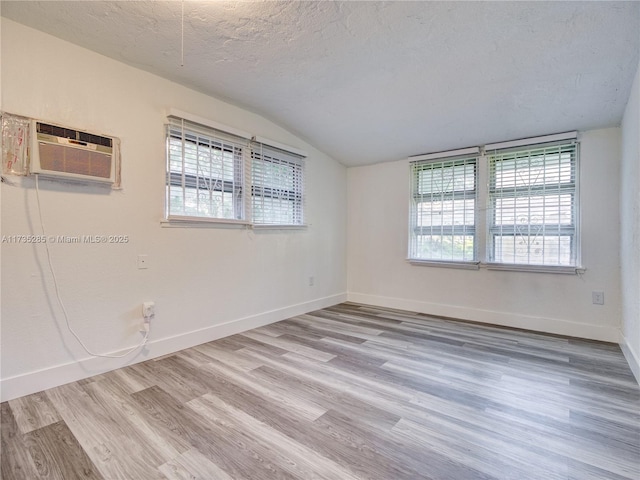 unfurnished room with a wall mounted air conditioner, lofted ceiling, hardwood / wood-style floors, and a textured ceiling