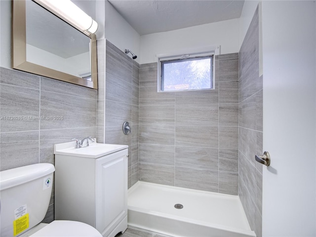 bathroom featuring vanity, a tile shower, tile walls, and toilet