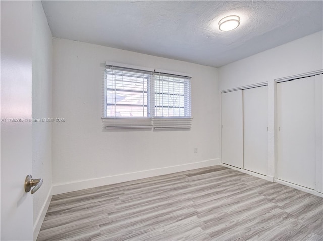 unfurnished bedroom featuring two closets, a textured ceiling, and light hardwood / wood-style flooring