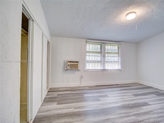 unfurnished bedroom with a closet, an AC wall unit, light hardwood / wood-style flooring, and a textured ceiling