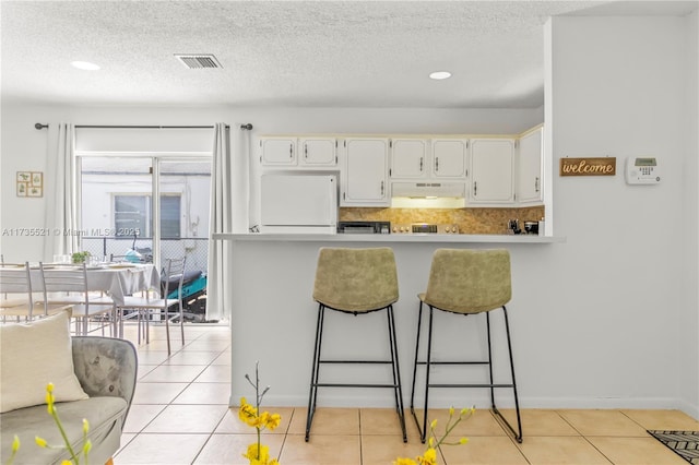 kitchen featuring light tile patterned floors, white cabinetry, backsplash, white refrigerator, and a textured ceiling