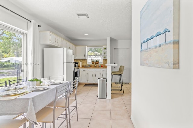 kitchen with white cabinetry, white fridge, light tile patterned floors, a textured ceiling, and decorative backsplash