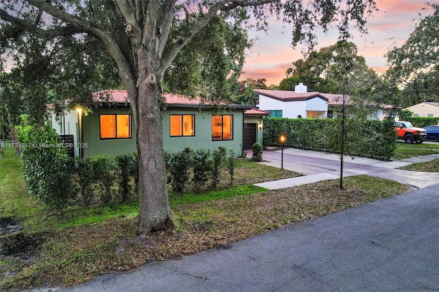 exterior space featuring a garage, concrete driveway, a chimney, a tiled roof, and stucco siding