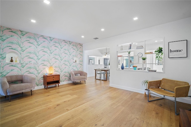 sitting room with light wood finished floors, recessed lighting, an accent wall, baseboards, and wallpapered walls