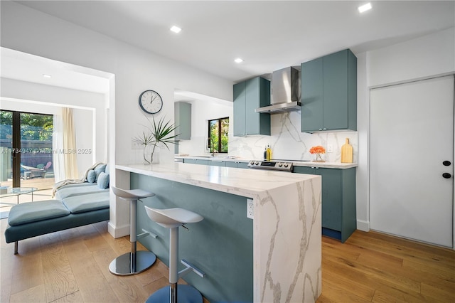 kitchen with a breakfast bar, light stone counters, decorative backsplash, kitchen peninsula, and wall chimney exhaust hood