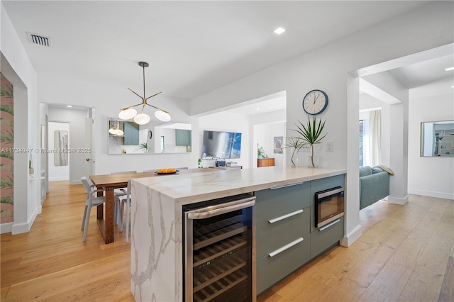 kitchen featuring beverage cooler, visible vents, light wood-type flooring, stainless steel microwave, and pendant lighting