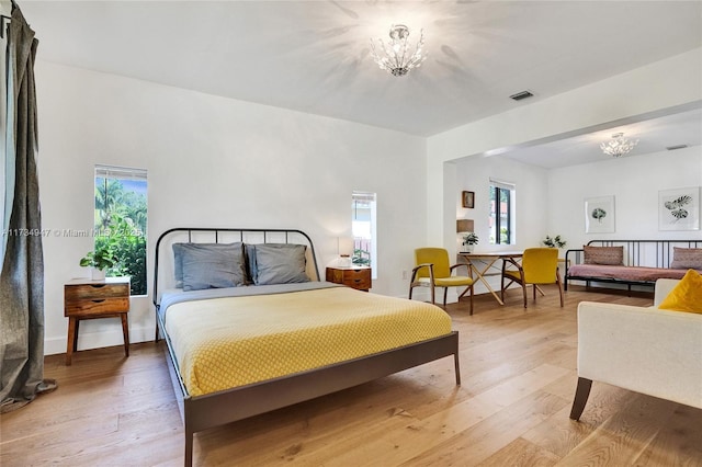 bedroom with baseboards, light wood-style floors, visible vents, and an inviting chandelier