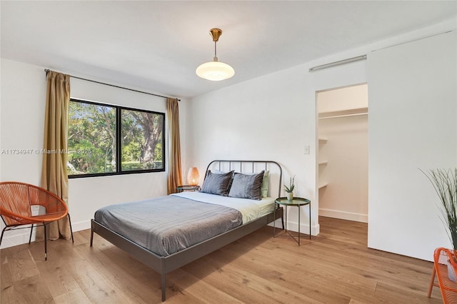 bedroom featuring light wood-style flooring, baseboards, and a spacious closet