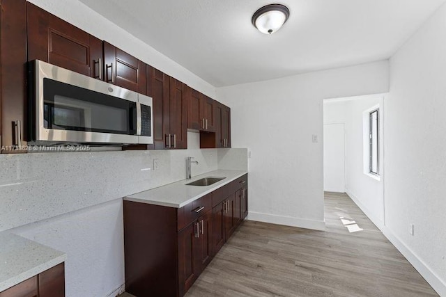 kitchen featuring light wood-type flooring, light stone countertops, sink, and backsplash