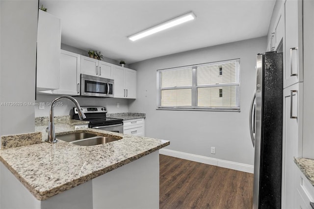 kitchen featuring dark wood-type flooring, appliances with stainless steel finishes, kitchen peninsula, light stone countertops, and white cabinets