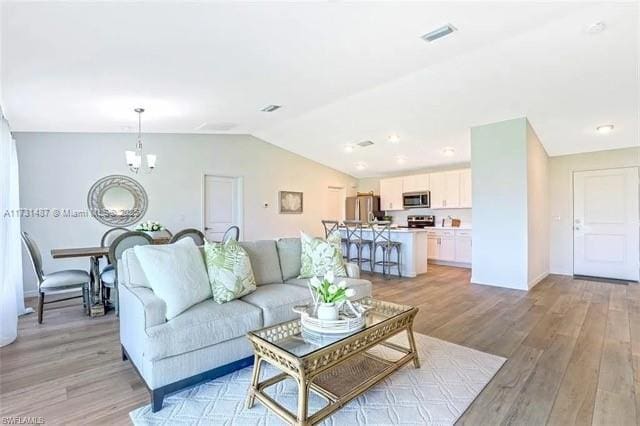 living room with lofted ceiling, an inviting chandelier, and light hardwood / wood-style flooring