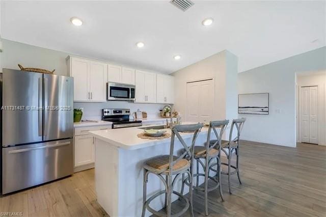 kitchen with vaulted ceiling, white cabinetry, sink, stainless steel appliances, and a center island with sink