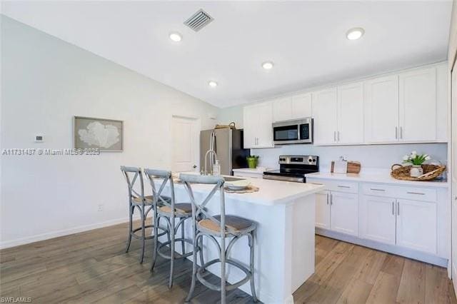 kitchen with a breakfast bar, appliances with stainless steel finishes, white cabinetry, a center island with sink, and vaulted ceiling