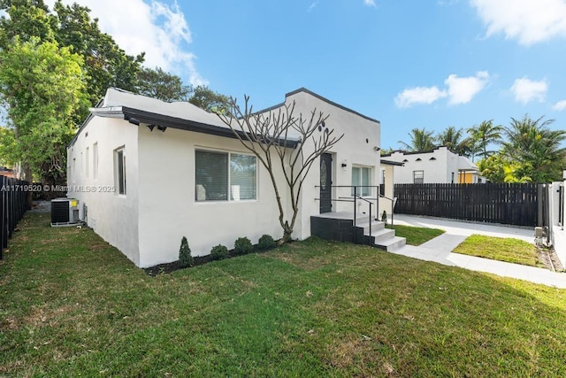 view of front facade with fence private yard, central AC, a front lawn, and stucco siding