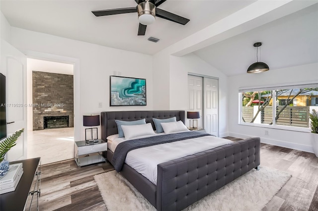 bedroom featuring a fireplace, lofted ceiling, visible vents, wood finished floors, and baseboards