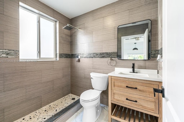 full bathroom featuring tiled shower, vanity, toilet, and tile walls