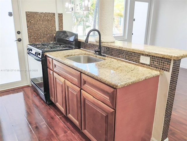 kitchen featuring sink, dark hardwood / wood-style floors, light stone countertops, black gas range, and decorative backsplash