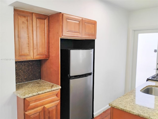 kitchen featuring hardwood / wood-style floors, stainless steel refrigerator, sink, backsplash, and light stone countertops