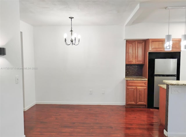 kitchen with dark hardwood / wood-style floors, stainless steel refrigerator, backsplash, hanging light fixtures, and an inviting chandelier