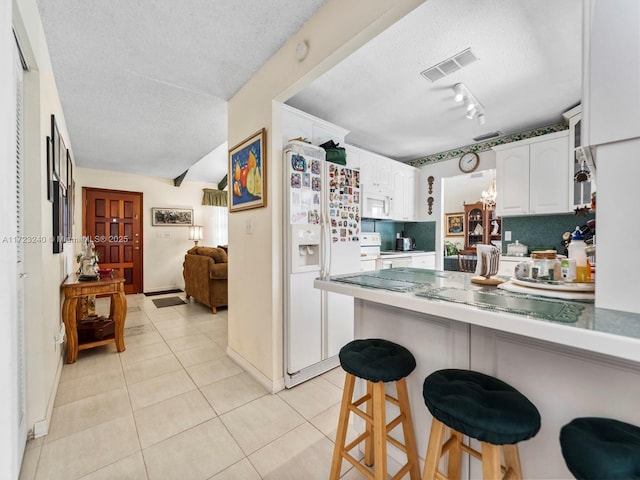 kitchen with a kitchen bar, a textured ceiling, light tile patterned floors, white appliances, and white cabinets