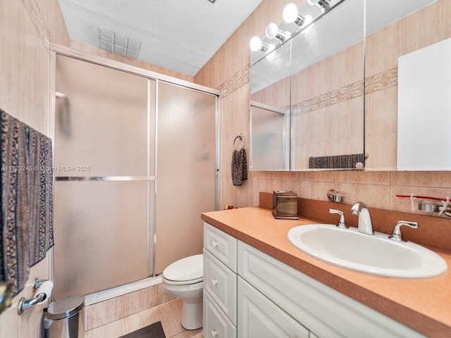 bathroom featuring walk in shower, vanity, toilet, and tile walls