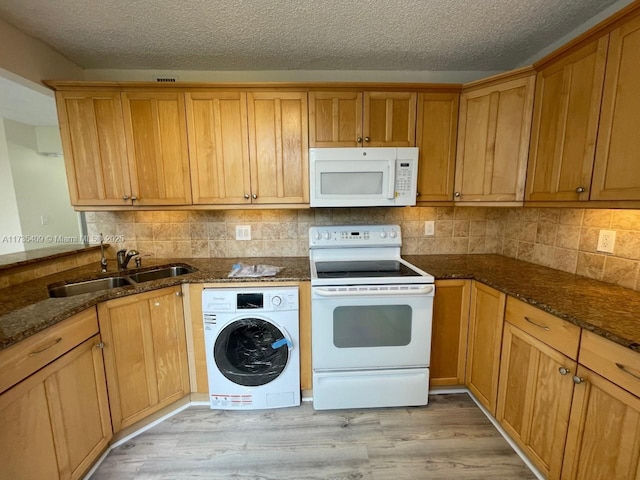 kitchen with white appliances, dark stone counters, washer / clothes dryer, and sink