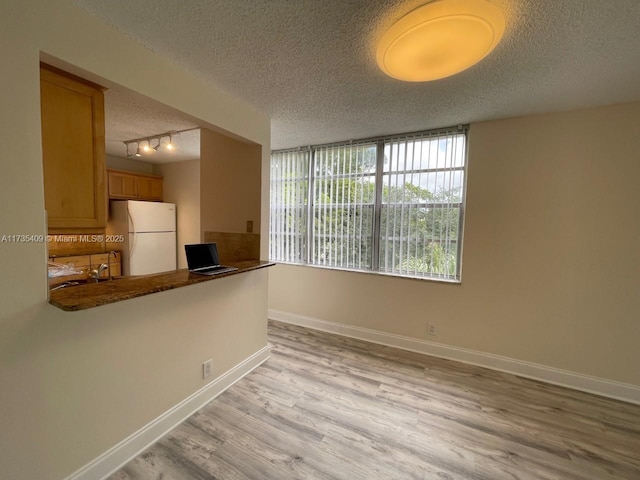 kitchen with white refrigerator, track lighting, a textured ceiling, kitchen peninsula, and light wood-type flooring