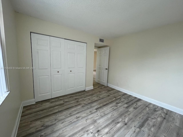 unfurnished bedroom featuring hardwood / wood-style floors, a closet, and a textured ceiling