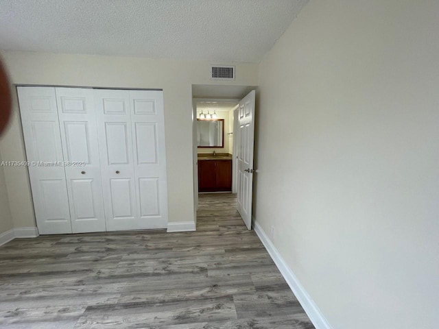 unfurnished bedroom featuring sink, light hardwood / wood-style floors, a closet, and a textured ceiling