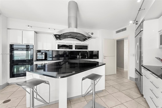 kitchen with white cabinetry, island range hood, a breakfast bar area, and black double oven