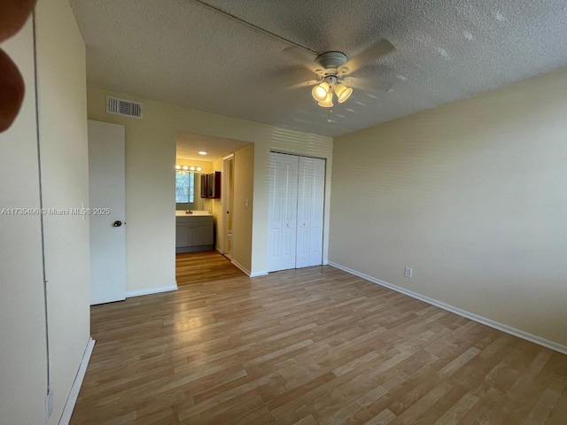 unfurnished bedroom with a closet, ensuite bath, a textured ceiling, and light hardwood / wood-style flooring