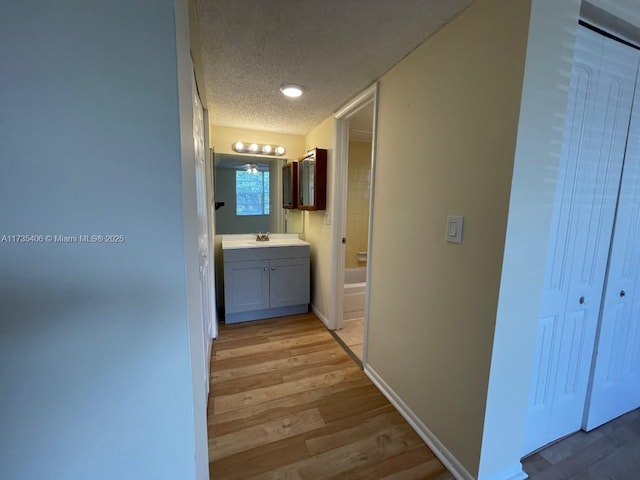 hall with light wood-type flooring, sink, and a textured ceiling