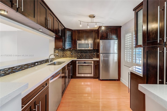 kitchen with sink, backsplash, dark brown cabinetry, stainless steel appliances, and light wood-type flooring