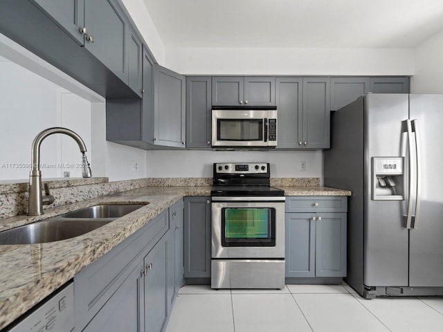 kitchen with stainless steel appliances, light stone countertops, sink, and gray cabinetry