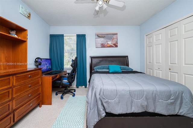 bedroom featuring a closet, light carpet, a textured ceiling, and a ceiling fan