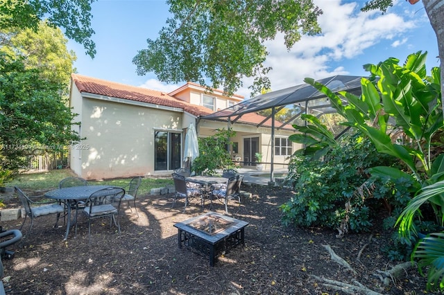 rear view of house with a lanai, a tiled roof, an outdoor fire pit, stucco siding, and a patio