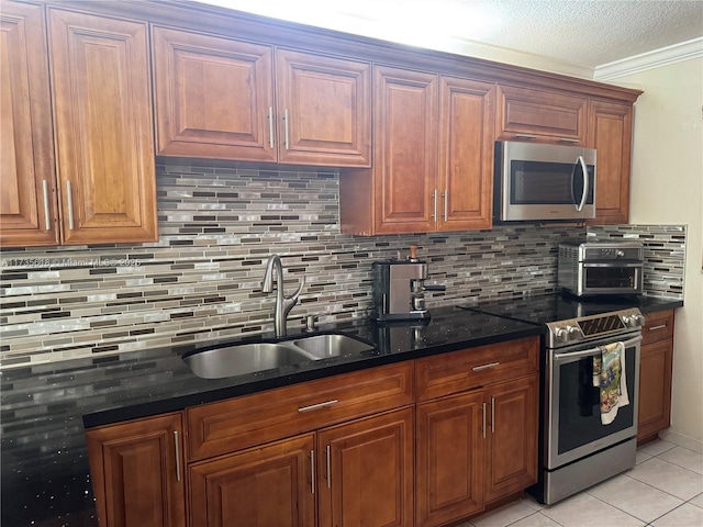 kitchen with brown cabinets, backsplash, appliances with stainless steel finishes, a sink, and dark stone counters