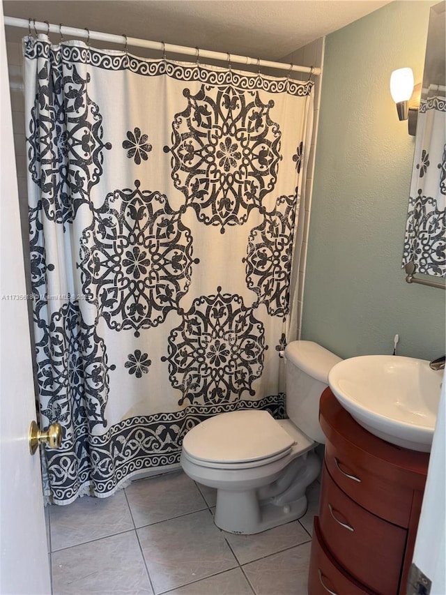 bathroom with tile patterned flooring, a textured wall, vanity, and toilet