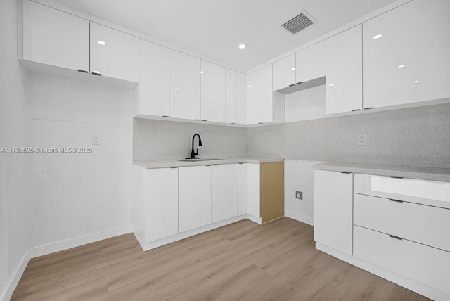 kitchen with tasteful backsplash, sink, light hardwood / wood-style flooring, and white cabinets