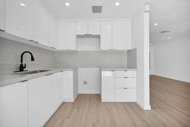 kitchen with white cabinetry, sink, backsplash, and light wood-type flooring