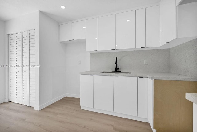 kitchen with decorative backsplash, sink, light hardwood / wood-style flooring, and white cabinets