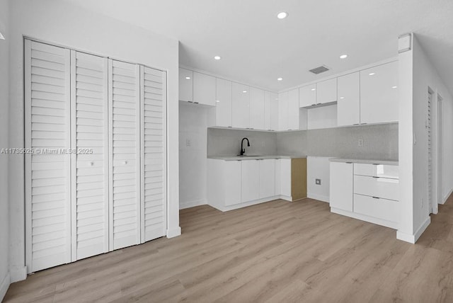 kitchen featuring white cabinetry, sink, backsplash, and light wood-type flooring