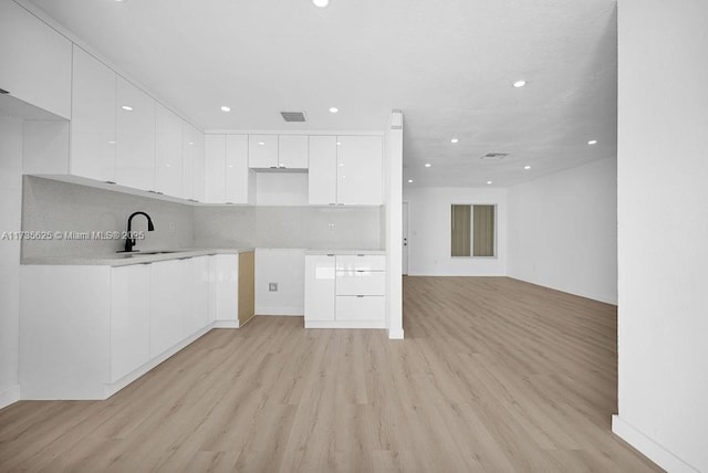 kitchen featuring white cabinetry, sink, backsplash, and light hardwood / wood-style floors