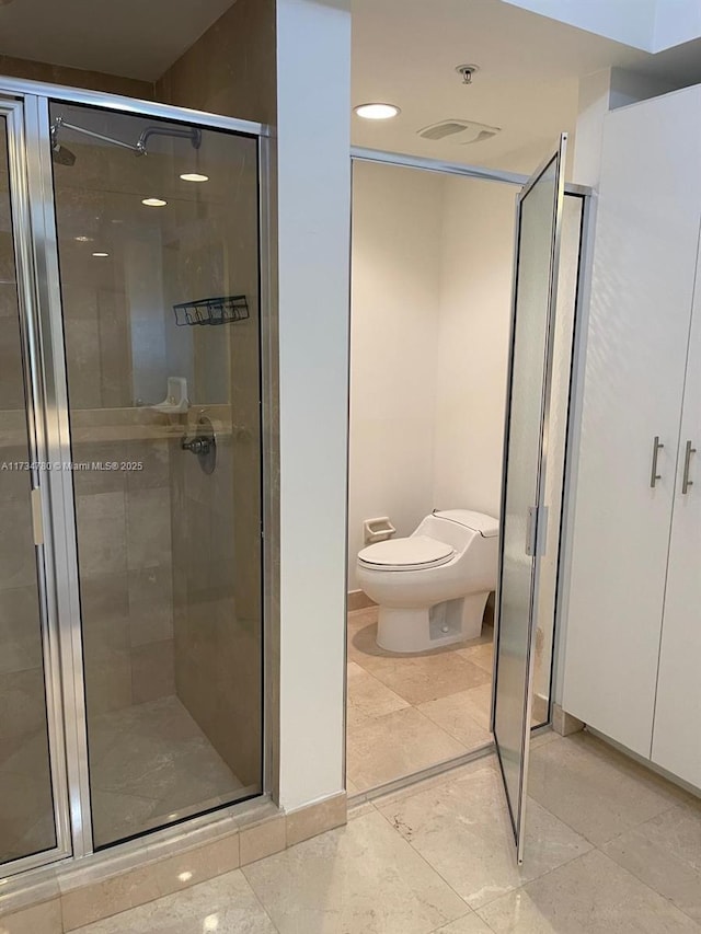 bathroom featuring a shower with door and toilet