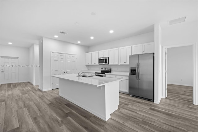 kitchen with sink, appliances with stainless steel finishes, white cabinets, a center island with sink, and light wood-type flooring