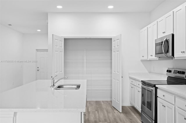 kitchen with sink, appliances with stainless steel finishes, white cabinetry, light hardwood / wood-style floors, and an island with sink