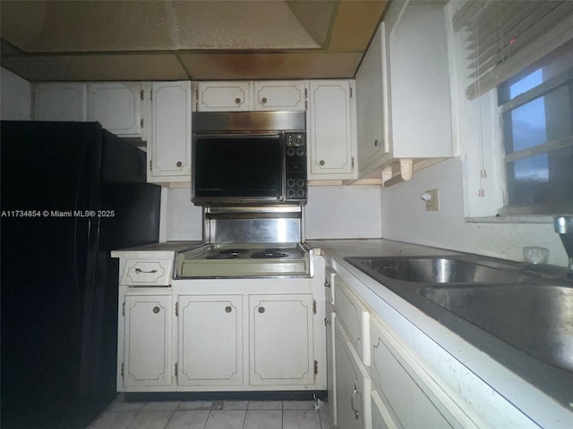 kitchen featuring light tile patterned floors, black appliances, sink, and white cabinets