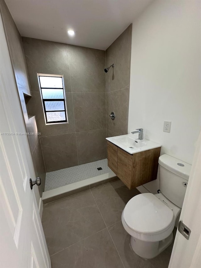 bathroom with tile patterned flooring, vanity, tiled shower, and toilet