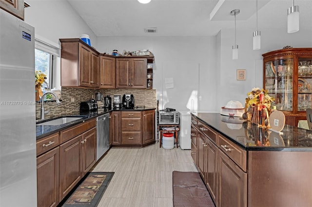 kitchen with appliances with stainless steel finishes, pendant lighting, tasteful backsplash, sink, and dark stone countertops