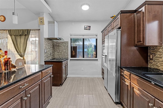 kitchen with pendant lighting, wall chimney range hood, appliances with stainless steel finishes, dark brown cabinetry, and tasteful backsplash